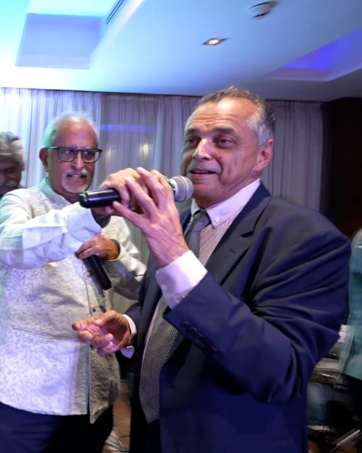 Ramesh Sadhwani holding a microphone out to a guest, who is singing into it